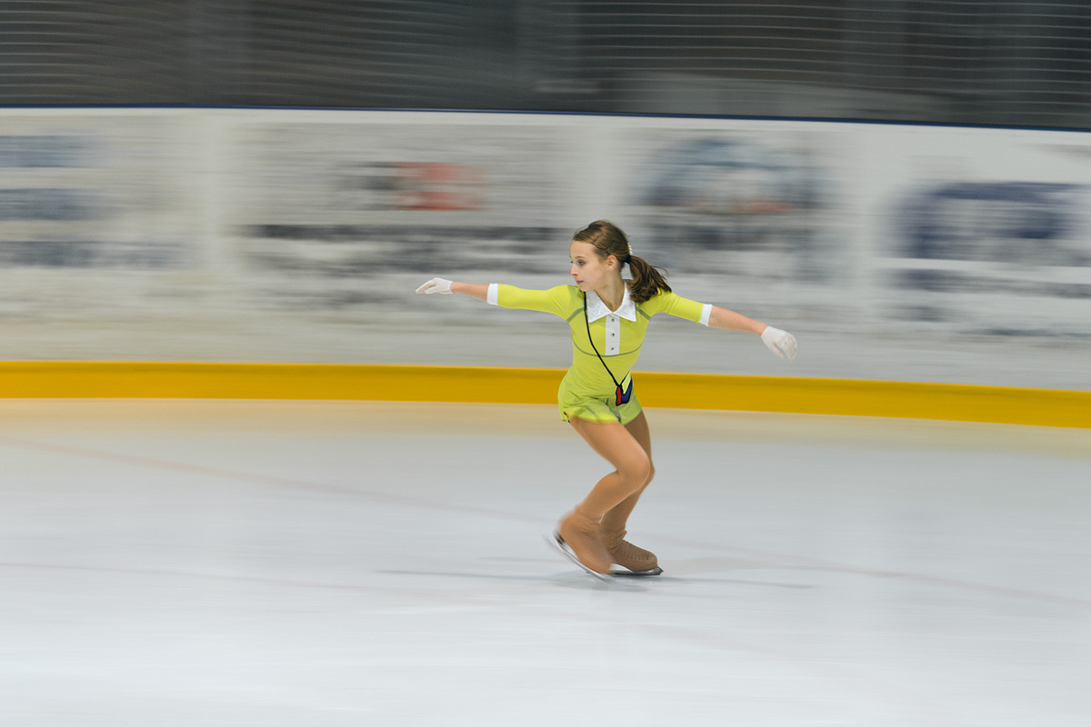 Girl figure skating on an ice rink with the background blurred by panning