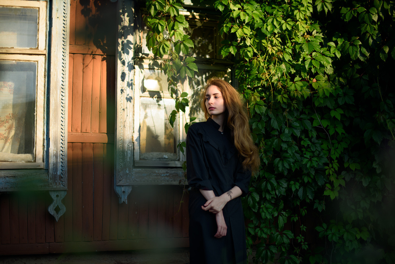 Young woman in a dark coat beside a garden gate with green leaves
