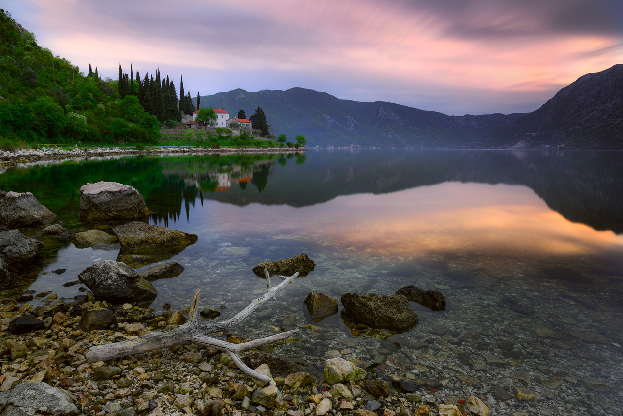 Calm mountain lake at dusk with rocks in the foreground and a village on the far shore