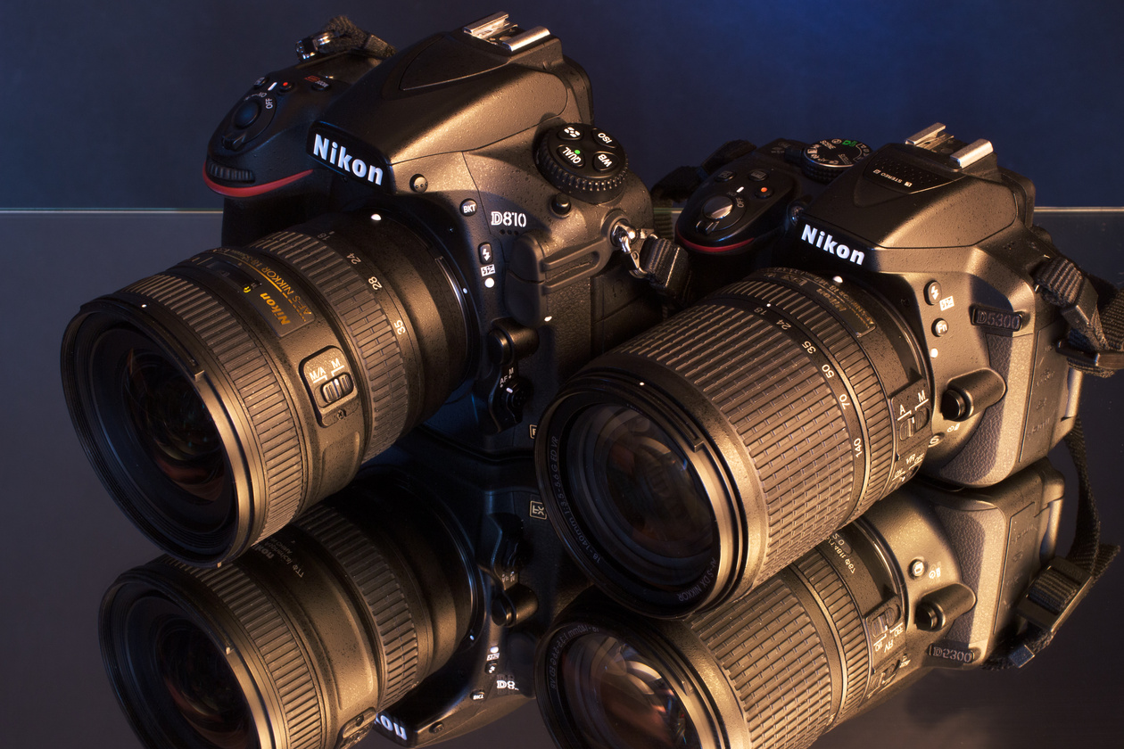 Two Nikon SLR cameras with zoom lenses reflected on a glossy surface