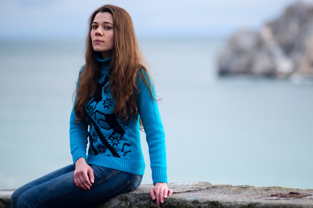 The same woman on the stone wall by the sea, framed tighter