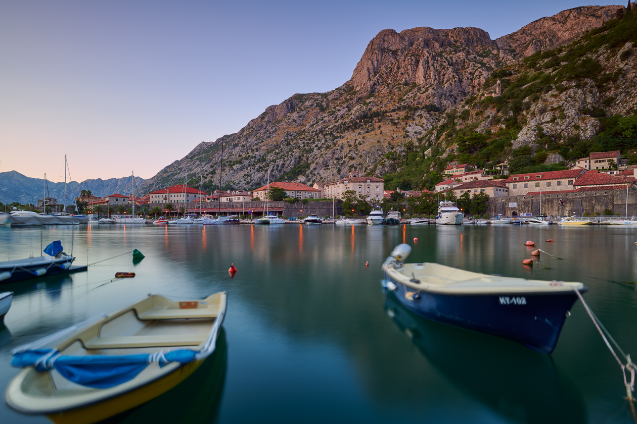 Small boats moored in a calm bay below a mountain and a waterfront town