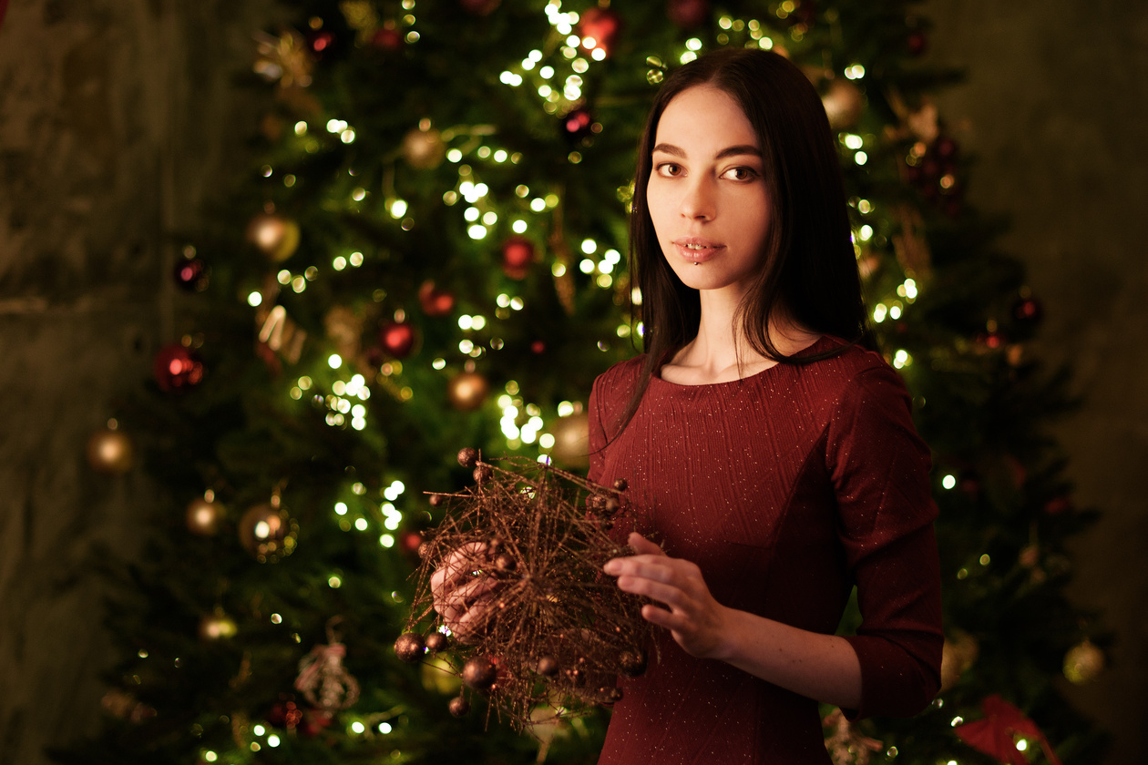 Young woman in a red dress holding a wreath in front of a lit Christmas tree