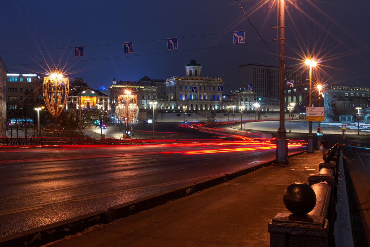 City street at night with light trails, lit streetlamps and a classical building