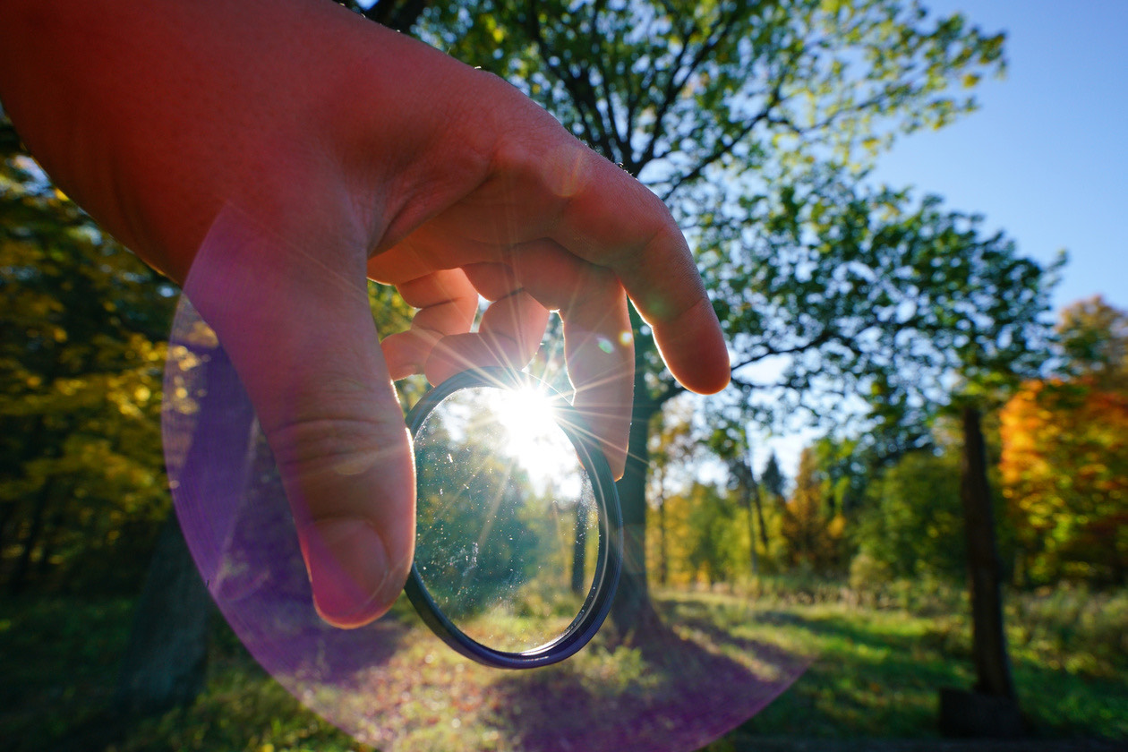 Hand holding a round lens filter up against the sun in a park