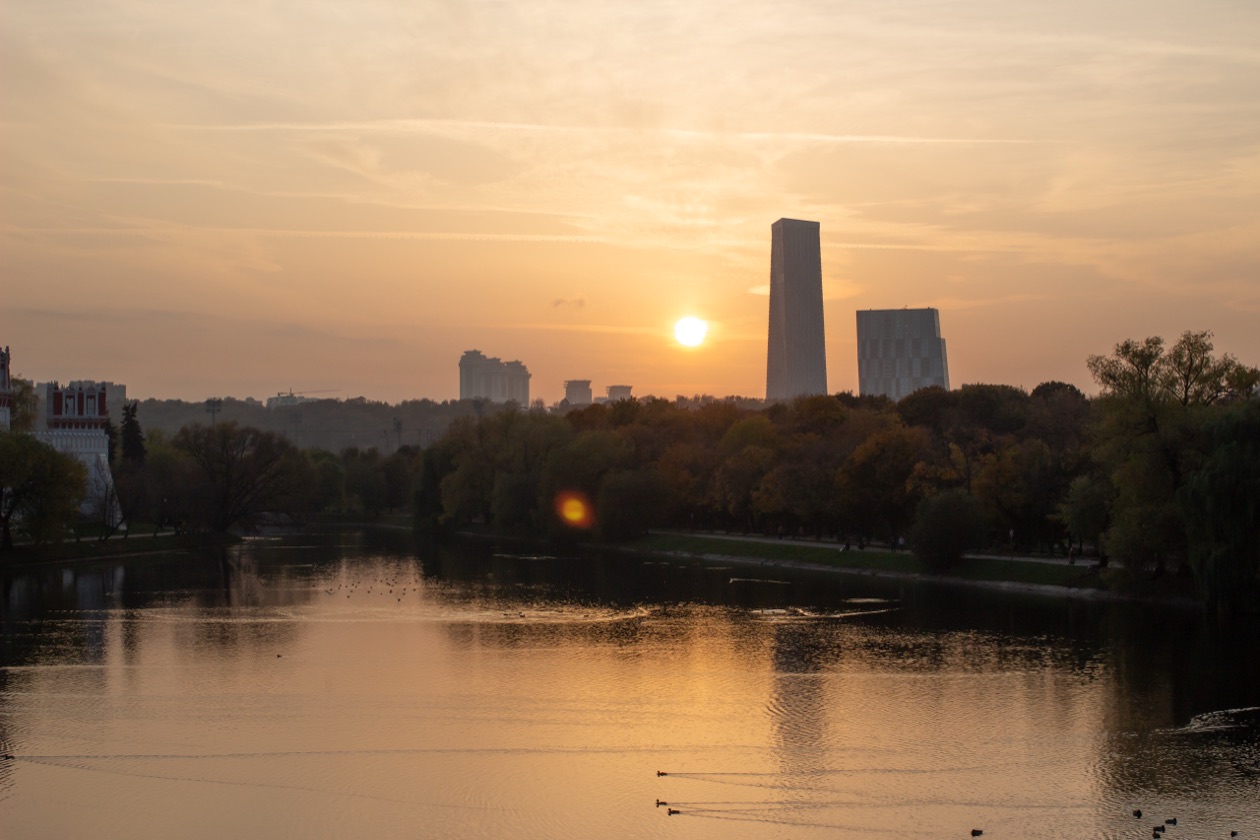 Sunset over a river with high-rise buildings and a flare spot in the frame