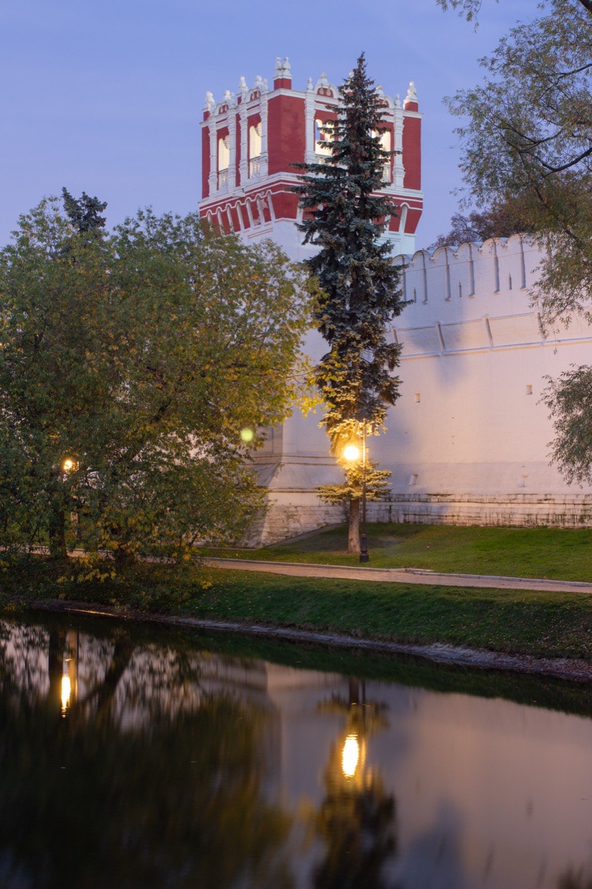 Monastery wall and red tower reflected in a pond at dusk