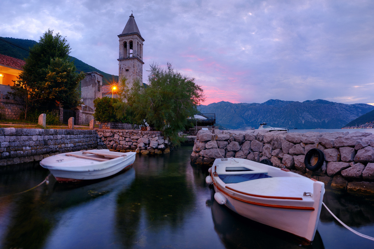 Boats moored in a small harbor below a church bell tower at dusk