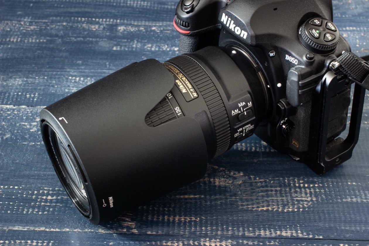 Nikon camera with a zoom lens fitted with a lens hood on a wooden surface
