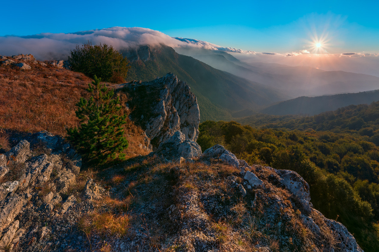 Mountain ridge above a valley with low clouds and the sun on the horizon