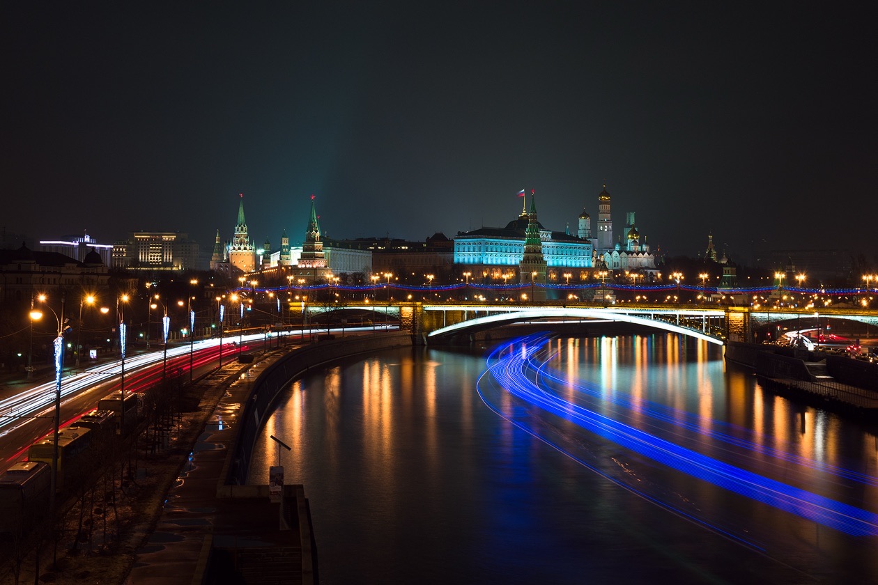 City river at night with the light trail of a passing boat and car headlight streaks