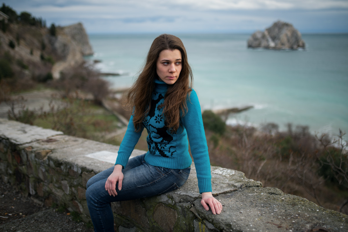 Young woman in a turquoise sweater sitting on a stone wall by the sea