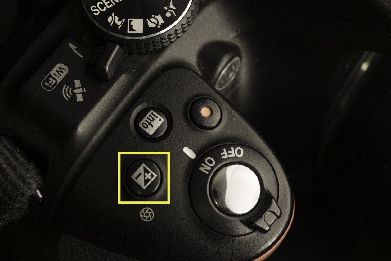 Top of a DSLR with the plus-minus exposure compensation button highlighted next to the power switch