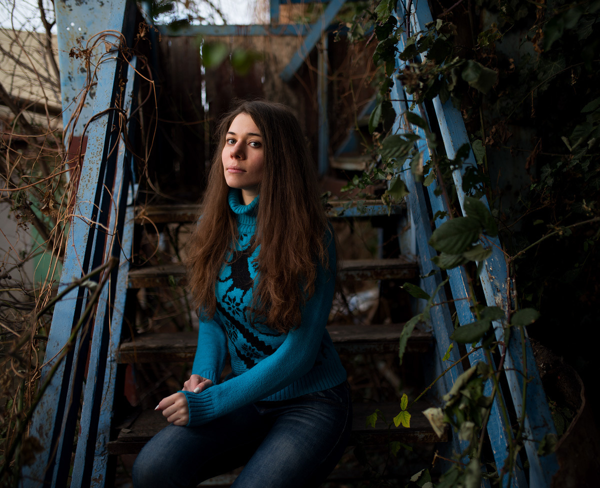 Young woman in a turquoise sweater sitting on old wooden stairs in deep shade