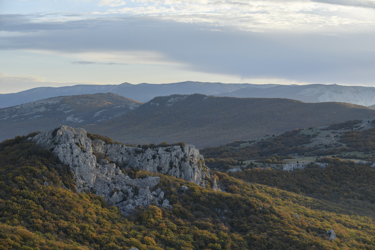 Rocky outcrop on a hillside of autumn shrubs below hazy mountain ridges