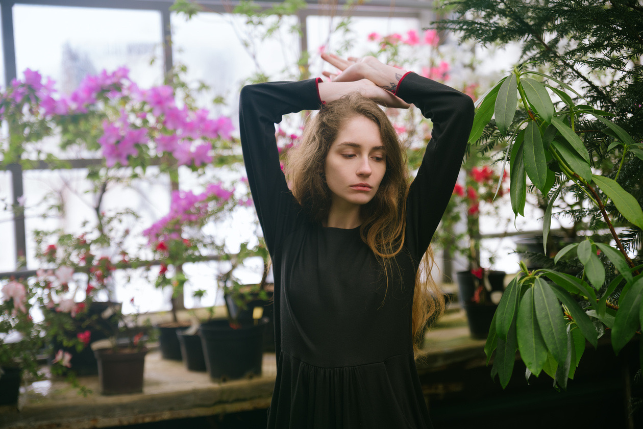 Young woman in black with raised arms in a greenhouse full of flowers against bright windows