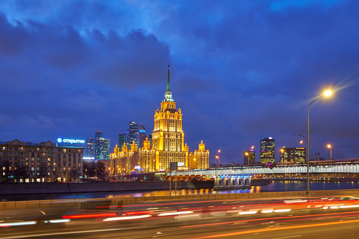 Lit high-rise building by a river at blue hour with car light trails on the embankment road