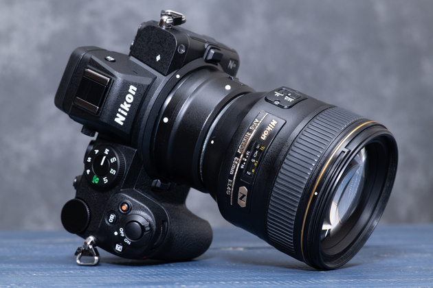 Mirrorless camera with a mount adapter and a fast 85 mm DSLR lens on a blue table