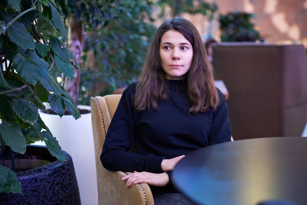 Young woman in a dark sweater sitting in a café armchair beside plants