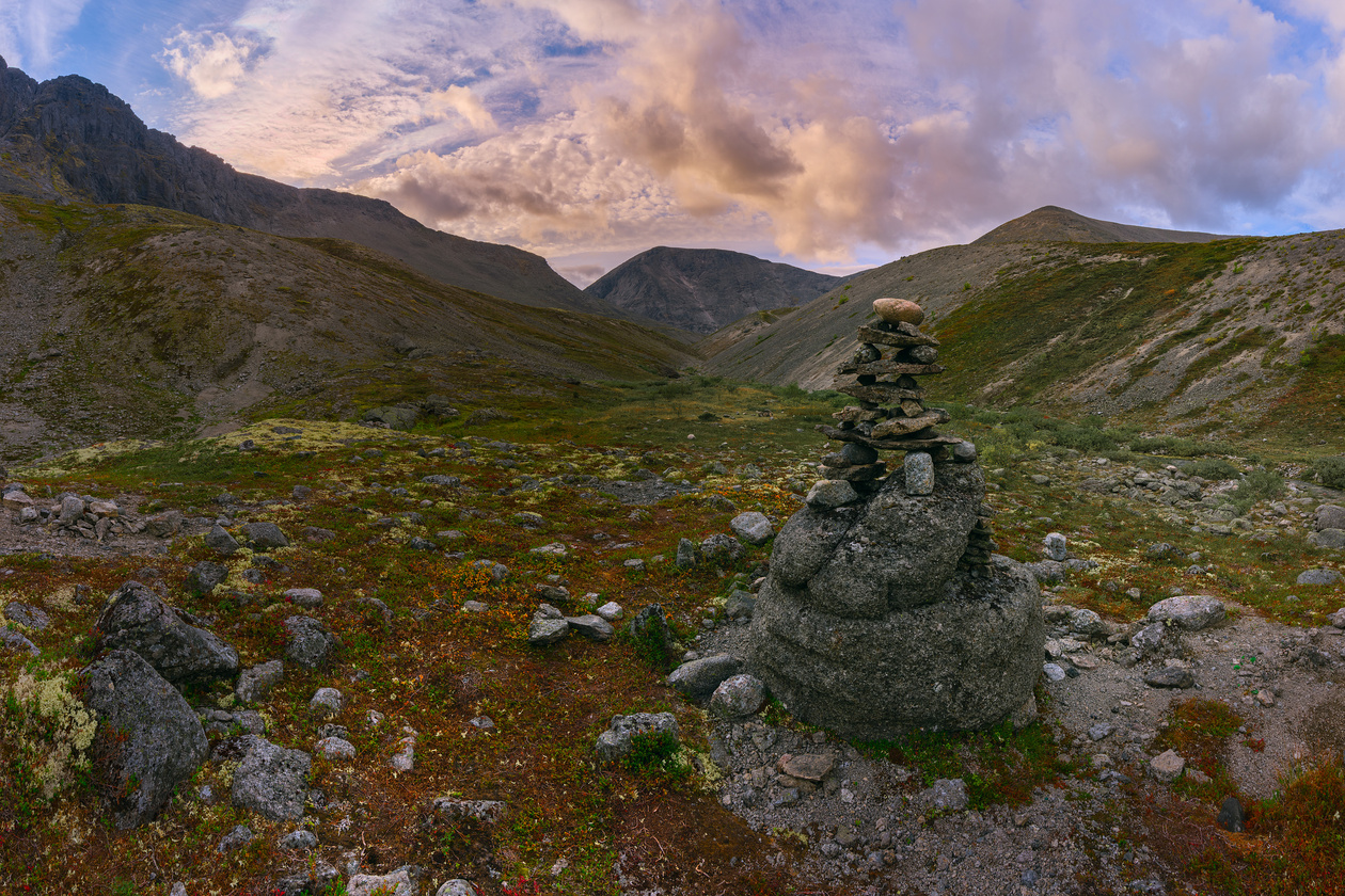 Mountain valley with a stone cairn in the foreground under a colorful evening sky