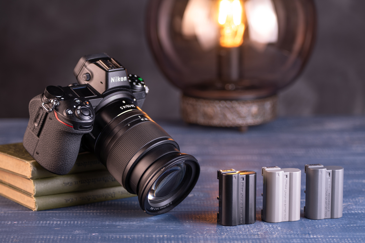 Mirrorless camera with a zoom lens next to three camera batteries on a blue table