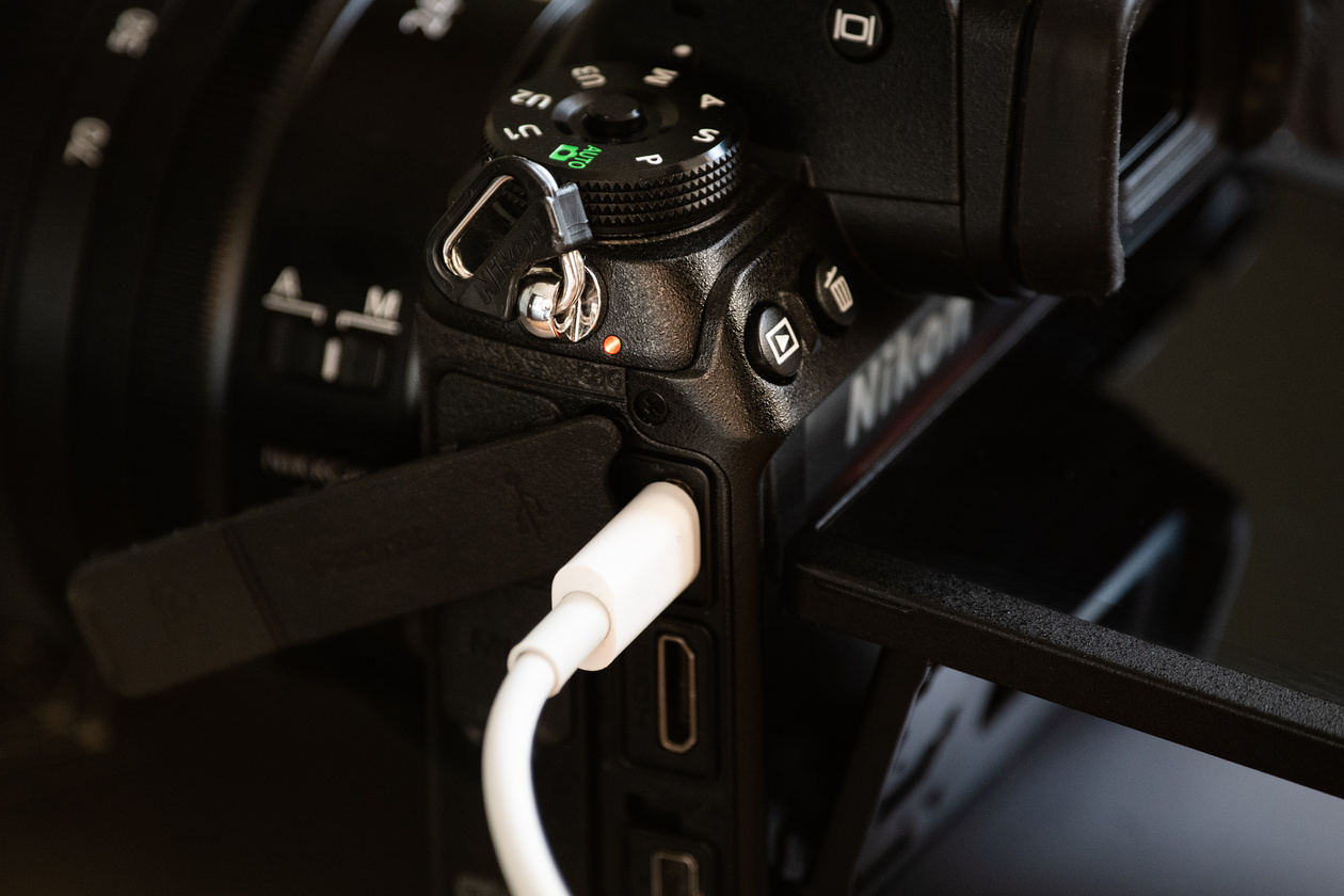 USB-C cable plugged into the side port of a mirrorless camera, with a small orange charging lamp lit