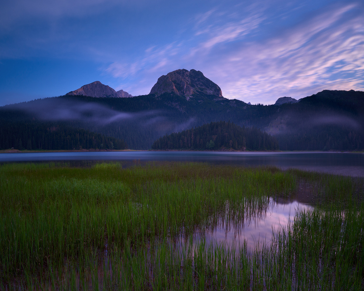 Mountain lake at twilight with reeds in the foreground and a smooth long-exposure sky