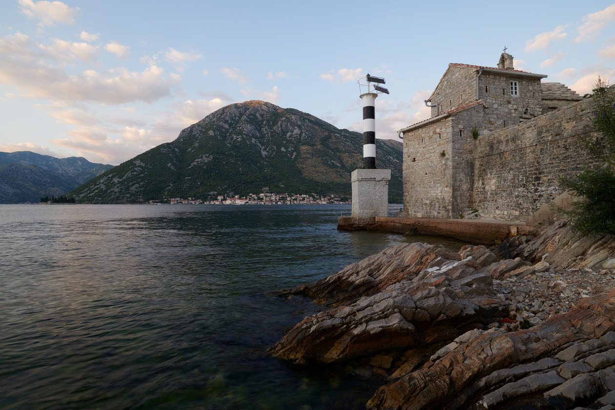 Stone building and striped lighthouse on a rocky shore of a bay, shot without a filter
