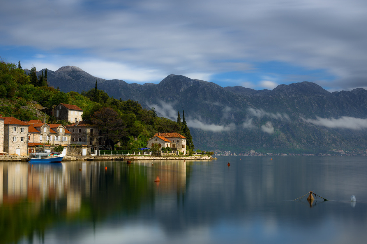 Bay with a waterside village and mountains under smoothly blurred clouds