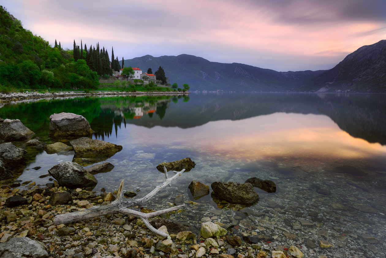 Calm lake at sunset with stones and driftwood in the foreground and glassy water