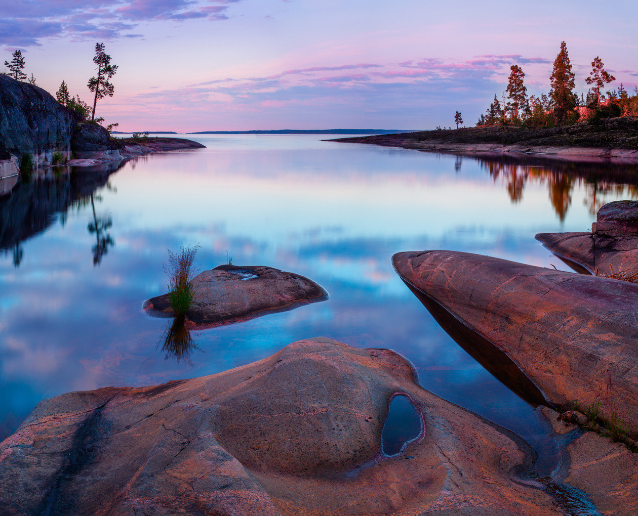 Rocky lakeshore at sunset with pink sky reflected in calm water
