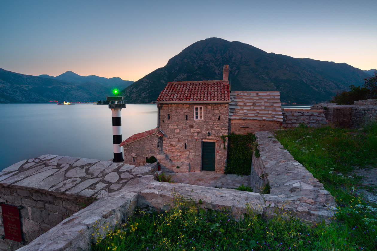 Small stone house with a lighthouse on a rocky shore at dusk