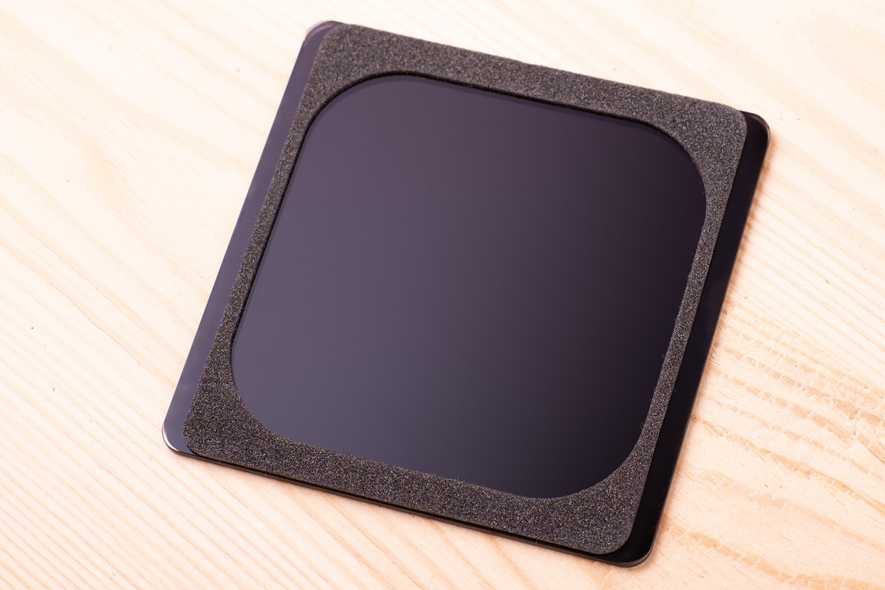 Square ND filter plate lying on a light wooden surface