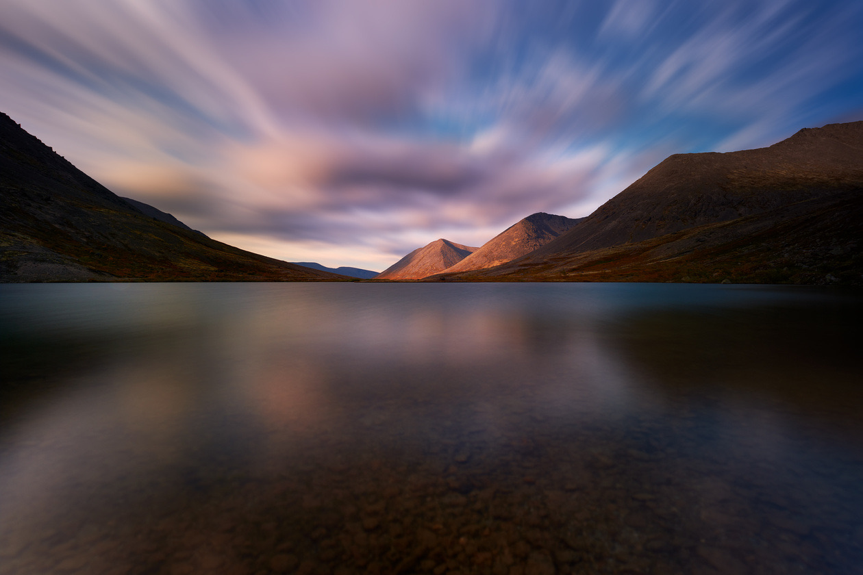 Mountain lake at dusk with clouds streaked across the sky by a very long exposure
