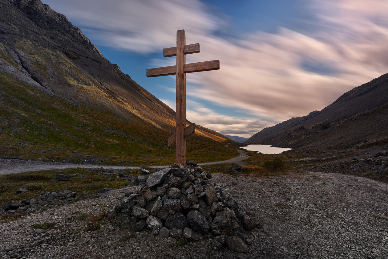 Wooden cross on a cairn of stones in a mountain valley with streaked clouds