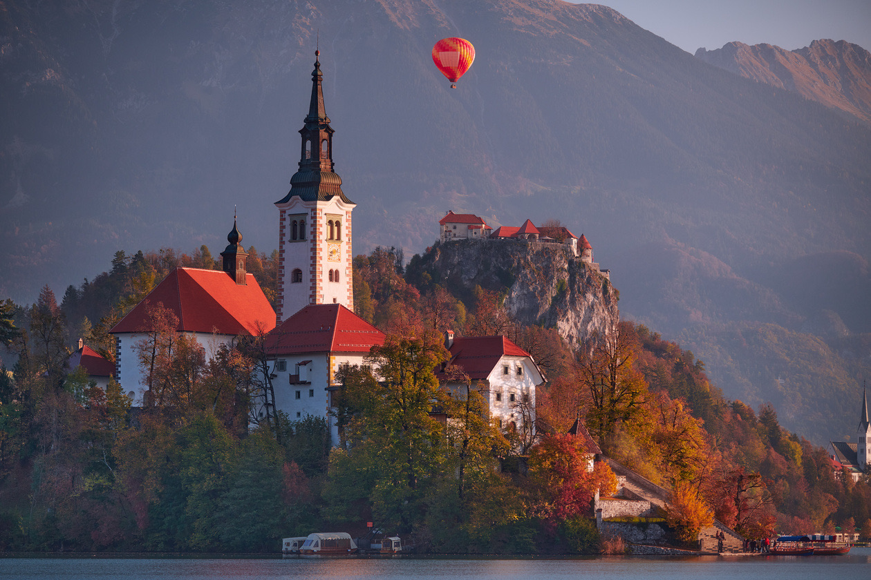 Church and castle on a cliff in autumn with a red hot-air balloon above