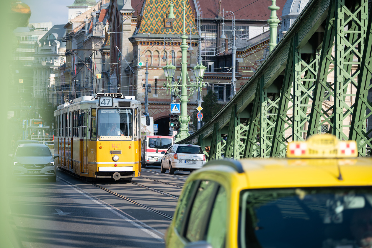 Yellow tram on a city bridge with a taxi in the foreground