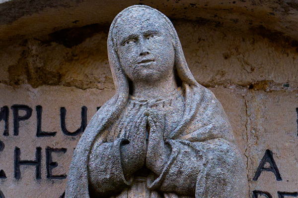 Sharp close-up of a weathered stone statue of the Virgin Mary in prayer