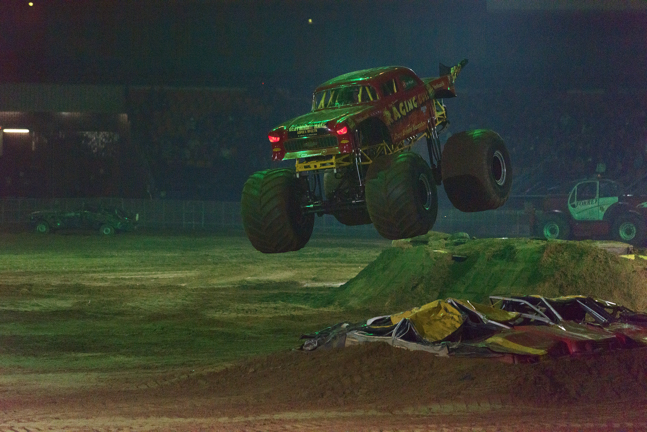 Monster truck jumping over a dirt ramp in a dark indoor arena
