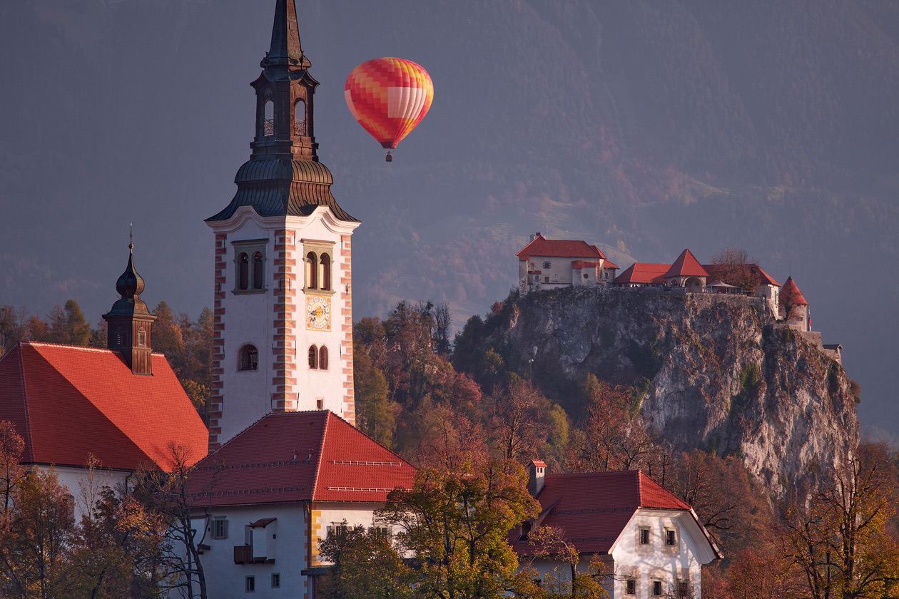 Church tower and castle on a cliff in autumn with a hot-air balloon behind